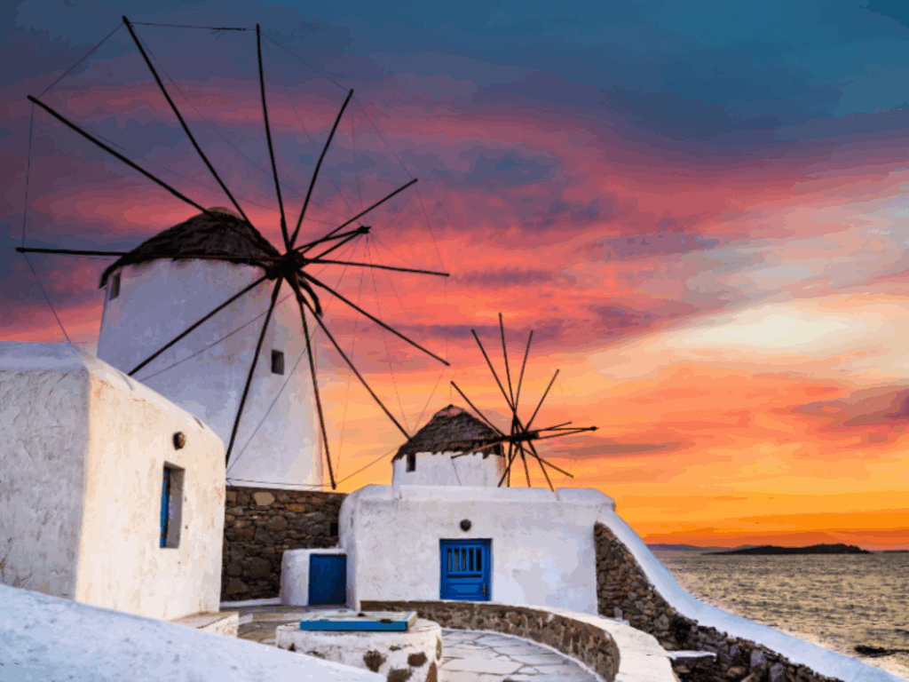 The windmills of Kato Mili in Mykonos against an intense sunset by the sea – an iconic symbol of the Cyclades.