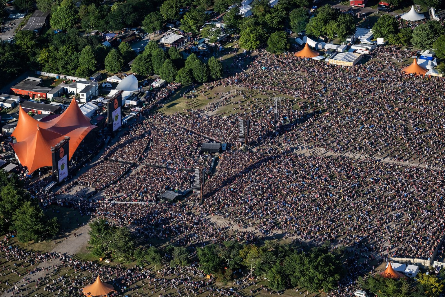 Roskilde Festival 2026 – Privatflug ab der Schweiz: Luftaufnahme einer riesigen Menschenmenge auf dem Festivalgelaende in Roskilde mit Bühnen und Zeltlandschaft.