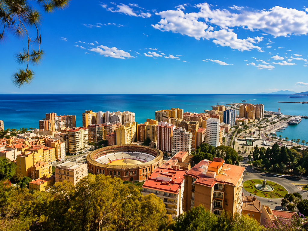 Panoramic view over Málaga on the Costa del Sol with bullring, modern skyline, marina and deep blue Mediterranean Sea under a cloudless sky.