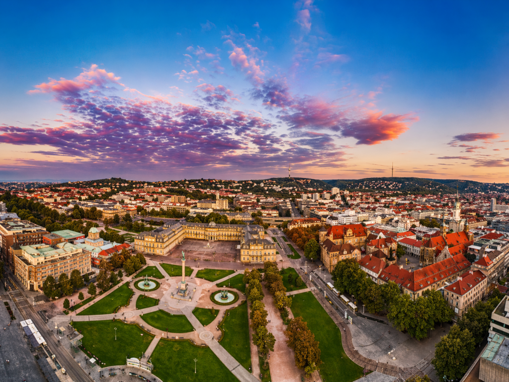 Panoramic view over the Schlossplatz in Stuttgart at sunset with the Jubilee Column, Old Castle, Collegiate Church and further skyline under a colorful evening sky.